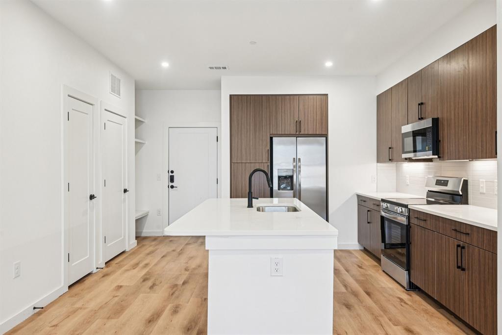 2016 South Ervay Street, Unit A1 Dallas, TX 75215 - Photo 8 of 35 Kitchen with stainless steel appliances, modern cabinets, a kitchen island with sink, light stone counters, and decorative backsplash