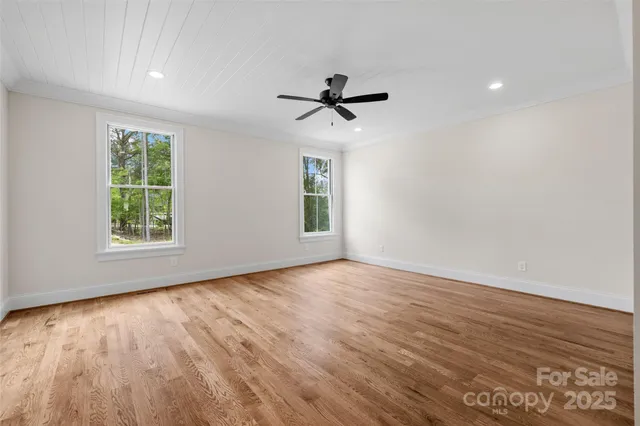 an empty room with wooden floor ceiling fan and windows