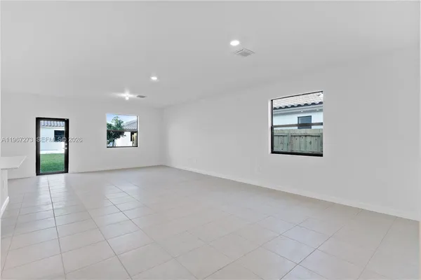 a view of an empty room and kitchen with window