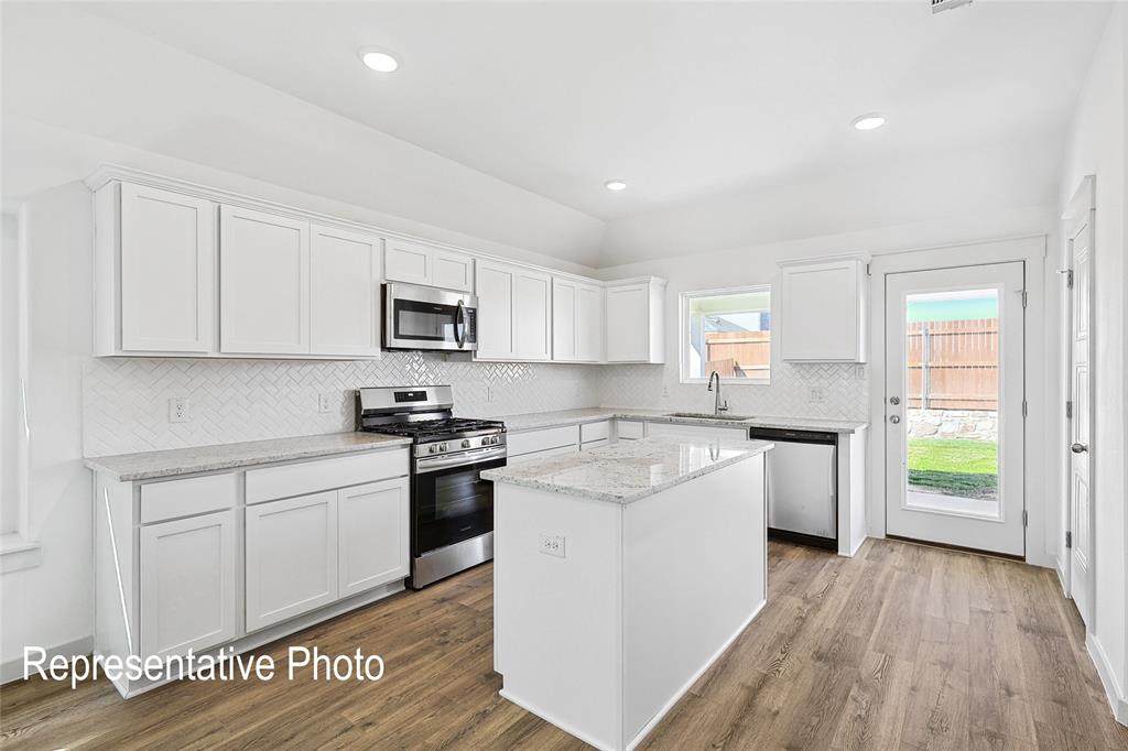 2709 Baker Farm Road Forney, TX 75126 - Photo 2 of 10 Bright kitchen featuring a central island, white cabinetry, stainless steel appliances, wood-finish flooring, and a subway tile backsplash