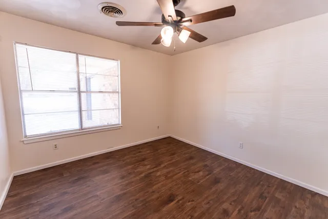 an empty room with wooden floor fan and windows