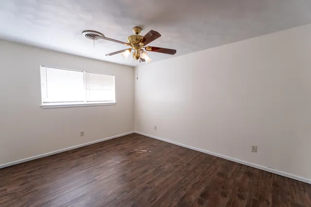 an empty room with wooden floor fan and windows