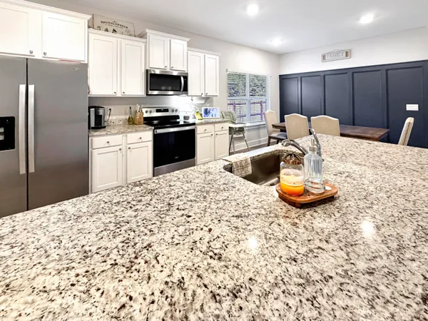 a kitchen with stainless steel appliances kitchen island granite countertop a refrigerator a stove a microwave oven a sink with a dining table and chairs