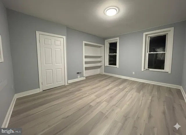 an empty room with wooden floor closet and windows