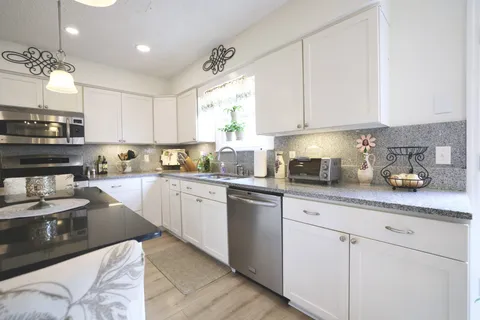 a kitchen with stainless steel appliances granite countertop a sink dishwasher stove and white cabinets with wooden floor