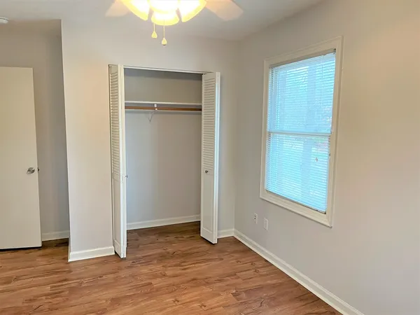 an empty room with wooden floor closet and windows