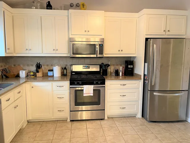 a kitchen with stainless steel appliances granite countertop a refrigerator stove a sink and dishwasher with white cabinets