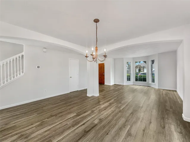 a view of an empty room with chandelier and wooden floor