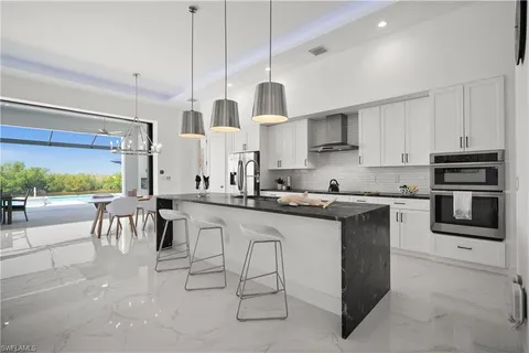 a kitchen with stainless steel appliances granite countertop a stove top oven a sink a dining table and chairs with white cabinets