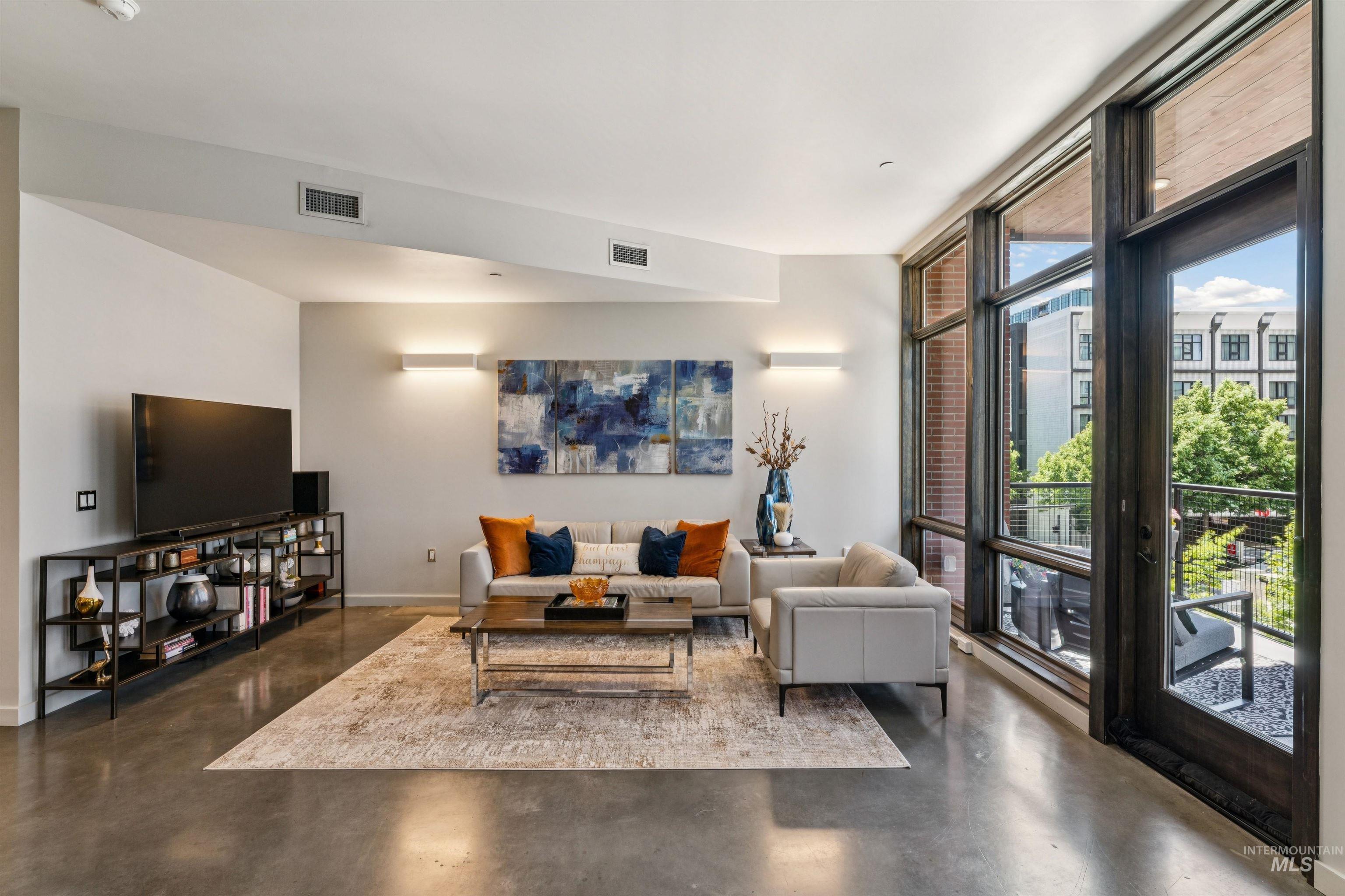 119 South 10th Street, Unit 307 Boise, ID 83702 - Photo 10 of 47 Spacious living area featuring polished concrete flooring, extensive floor-to-ceiling windows, and a glass-paneled door opening to a private balcony
