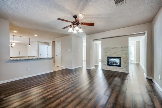a view of an empty room with wooden floor and a kitchen