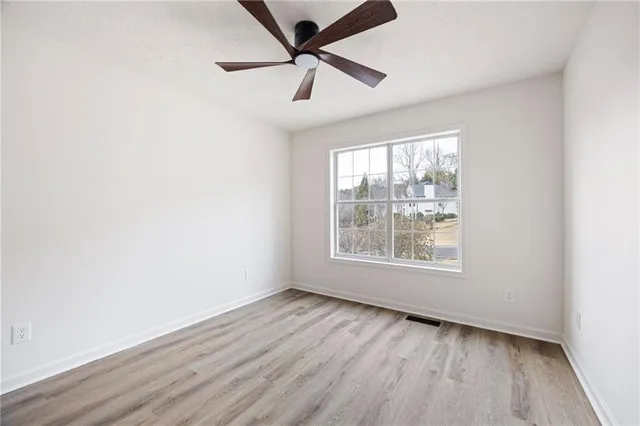 an empty room with wooden floor chandelier fan and windows