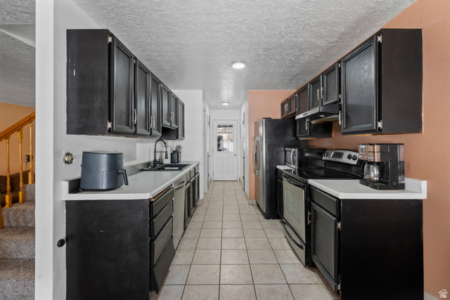 165 Pheasantbrook Drive Centerville, UT 84014 - Photo 6 of 30 Kitchen with dark cabinetry, stainless steel appliances, light countertops, a textured ceiling, and light tile patterned flooring