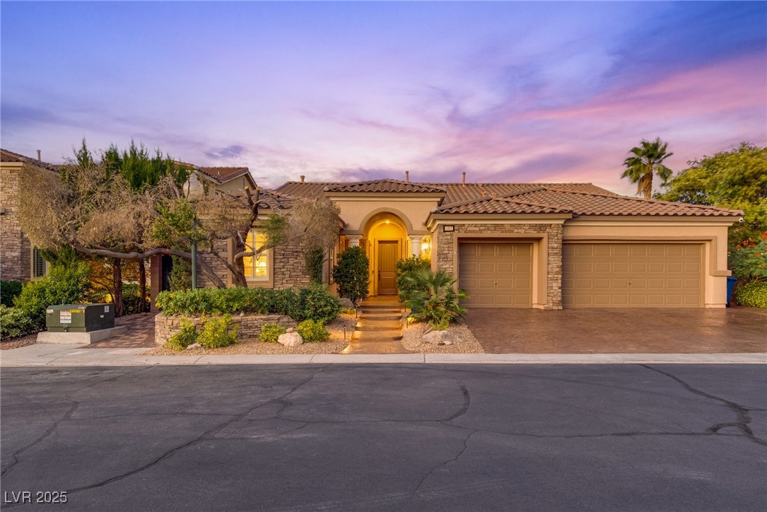 Mediterranean / spanish home with stone siding, a garage, driveway, a tiled roof, and stucco siding