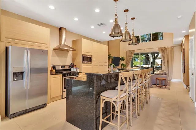 a dining room with stainless steel appliances kitchen island granite countertop a refrigerator a stove a kitchen island and chairs with wooden floor
