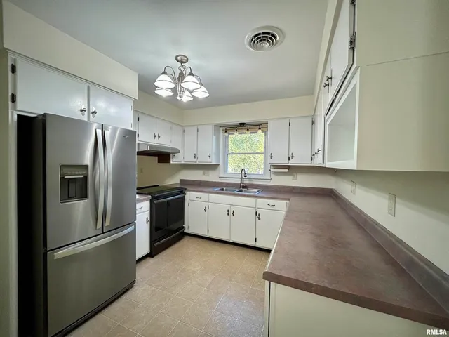 a kitchen with granite countertop a refrigerator oven a sink dishwasher and white cabinets