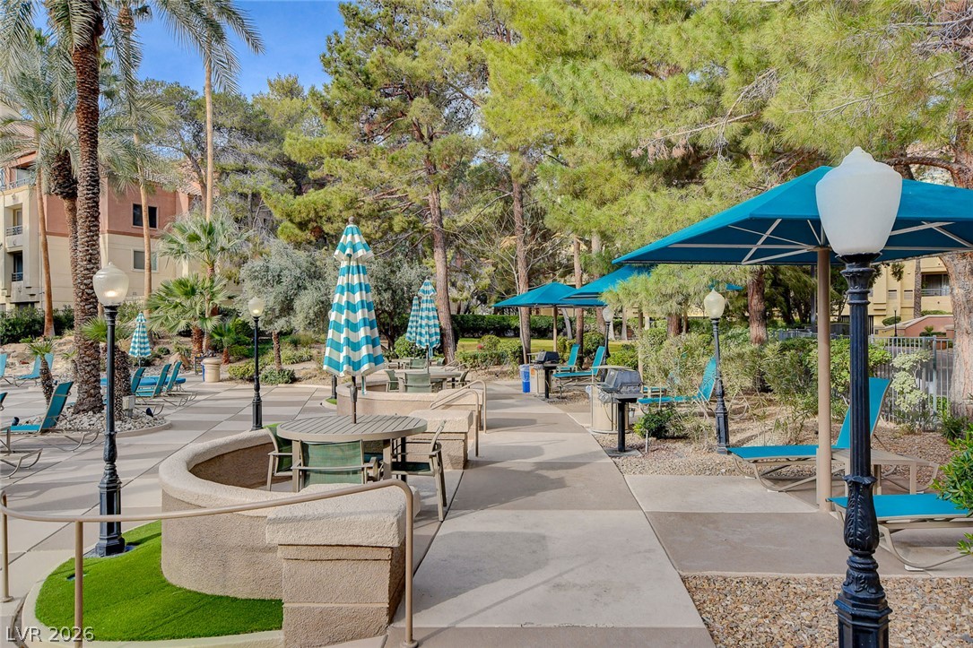230 East Flamingo Road, Unit 106 Las Vegas, NV 89169 - Photo 49 of 66 Patio dining beneath vibrant umbrellas offers a perfect setting for outdoor gatherings amidst lush landscaping.