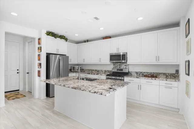 a kitchen with stainless steel appliances granite countertop a stove top oven a sink a refrigerator white cabinets and wooden floor