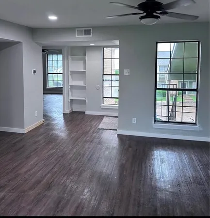 an empty room with wooden floor cabinet and windows