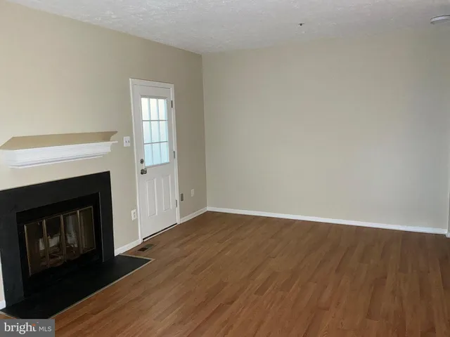 a view of an empty room with wooden floor and a fireplace