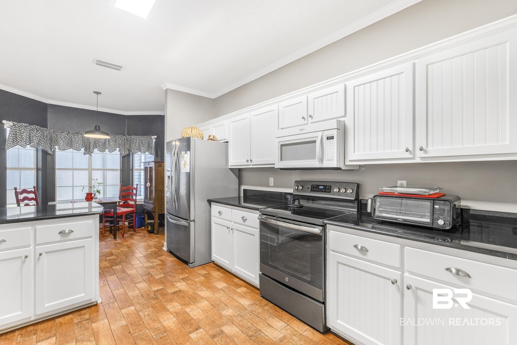 10603 Old Stage Road Stockton, AL 36579 - Photo 16 of 34 Kitchen featuring appliances with stainless steel finishes, ornamental molding, white cabinets, hanging light fixtures, and light wood finished floors