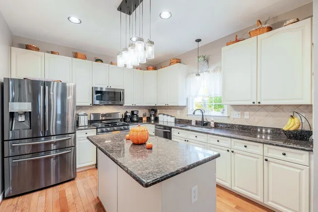 a kitchen with stainless steel appliances granite countertop a refrigerator a stove top oven a sink dishwasher and white cabinets with wooden floor