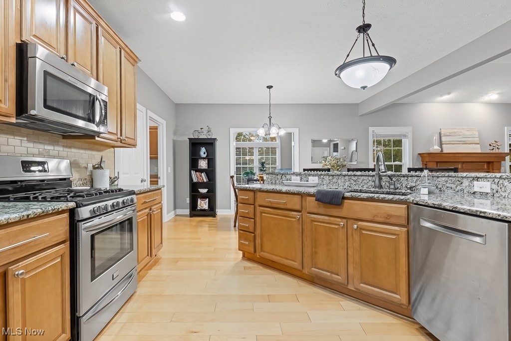 369 Eldridge Road Aurora, OH 44202 - Photo 7 of 50 Kitchen featuring appliances with stainless steel finishes, light wood-style flooring, tasteful backsplash, pendant lighting, and light stone counters