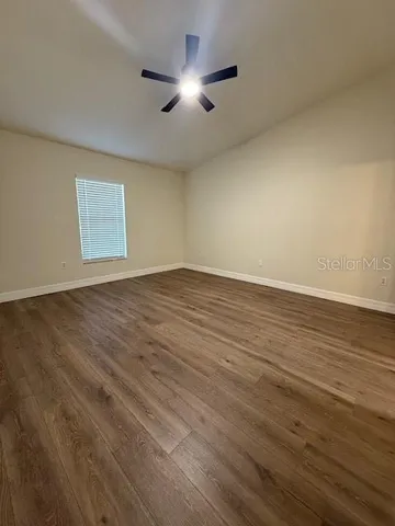 a view of an empty room with wooden floor and a ceiling fan