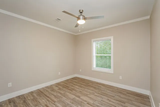an empty room with wooden floor chandelier fan and windows