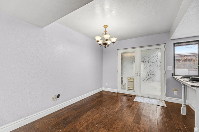 34 Benchmark Village Tooele, UT 84074 - Photo 8 of 35 Unfurnished dining area featuring a textured wall, suspended lighting, dark wood-style floors, french doors, and a textured ceiling
