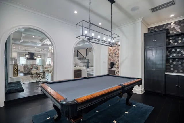 a room with pool table a chandelier and windows