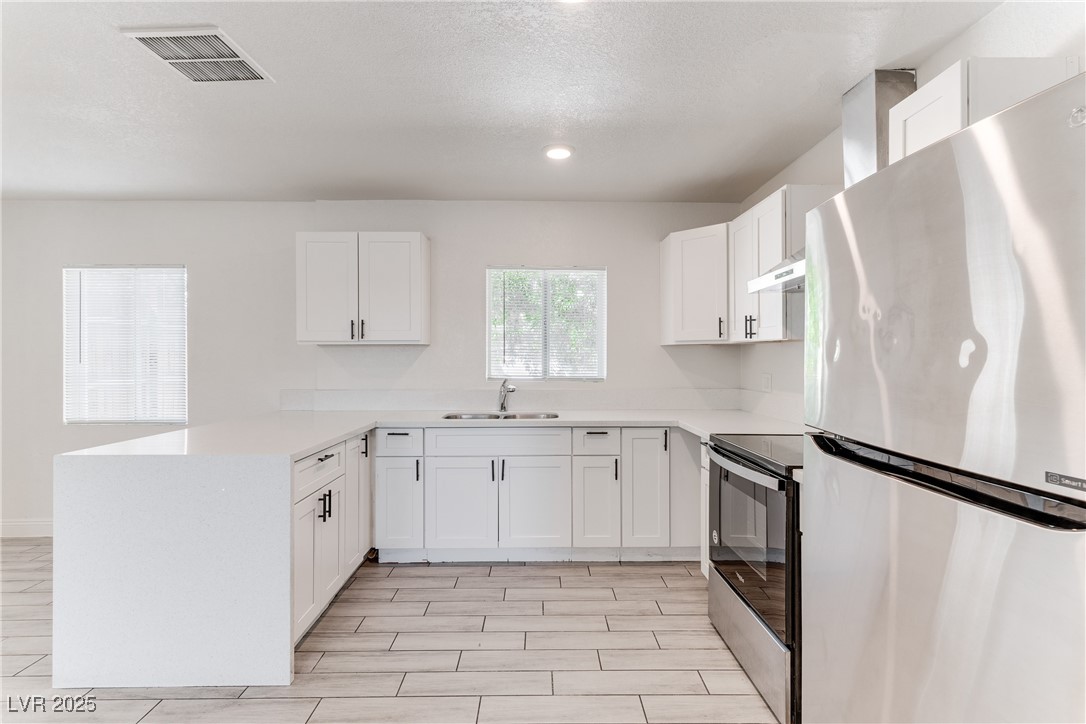 309 North 16th Street, Unit A Las Vegas, NV 89101 - Photo 2 of 23 Kitchen featuring stainless steel appliances, a peninsula, white cabinets, a textured ceiling, and light stone countertops