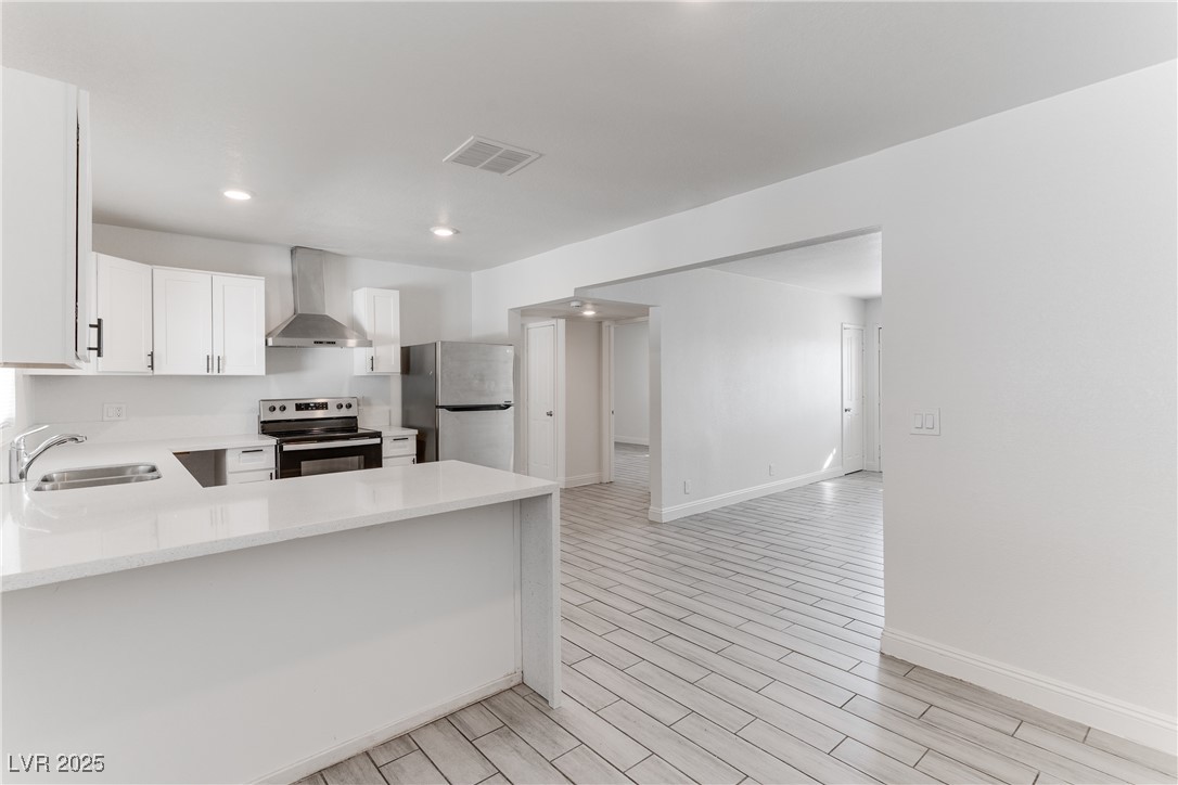309 North 16th Street, Unit A Las Vegas, NV 89101 - Photo 3 of 23 Kitchen with stainless steel appliances, wood finish floors, white cabinets, light stone counters, and wall chimney exhaust hood