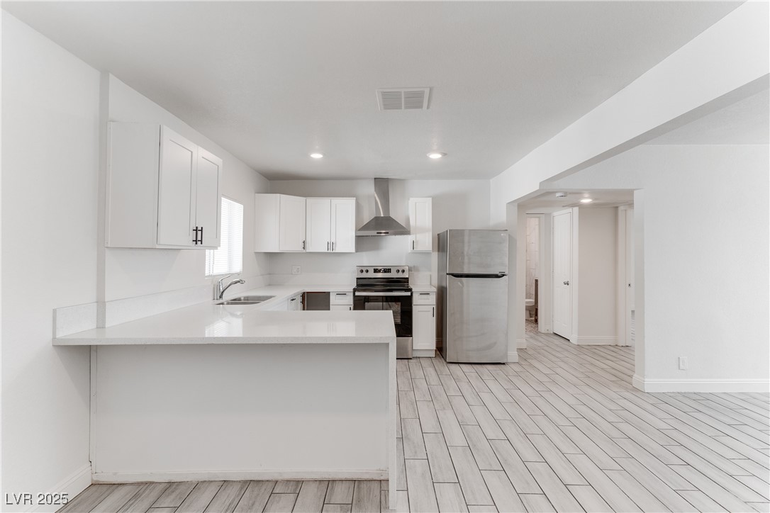 309 North 16th Street, Unit A Las Vegas, NV 89101 - Photo 10 of 23 Kitchen with stainless steel appliances, wall chimney range hood, a peninsula, white cabinets, and wood finish floors