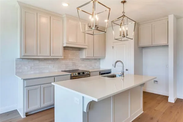 a kitchen with stainless steel appliances granite countertop a sink a stove a refrigerator and white cabinets with wooden floor