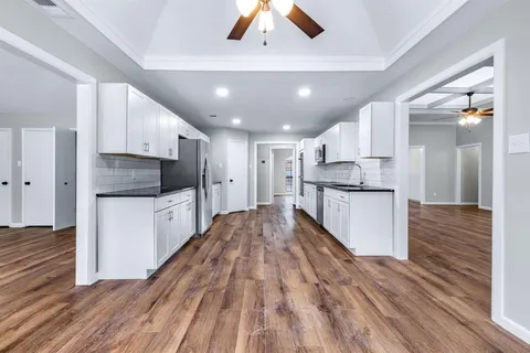 a kitchen with stainless steel appliances kitchen island granite countertop a stove a refrigerator and white cabinets with wooden floor