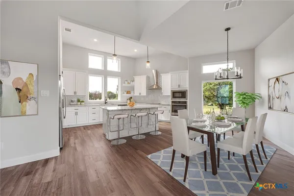 a room with stainless steel appliances kitchen island granite countertop a dining table chairs and white cabinets