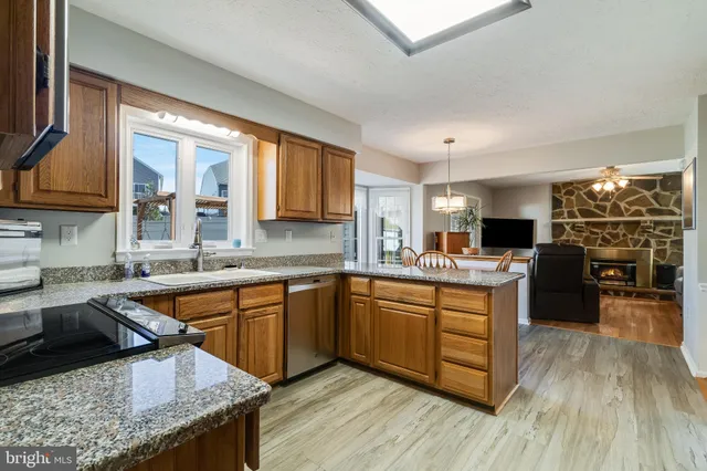 a kitchen with stainless steel appliances granite countertop wooden cabinets a sink dishwasher a stove and a refrigerator with wooden floor