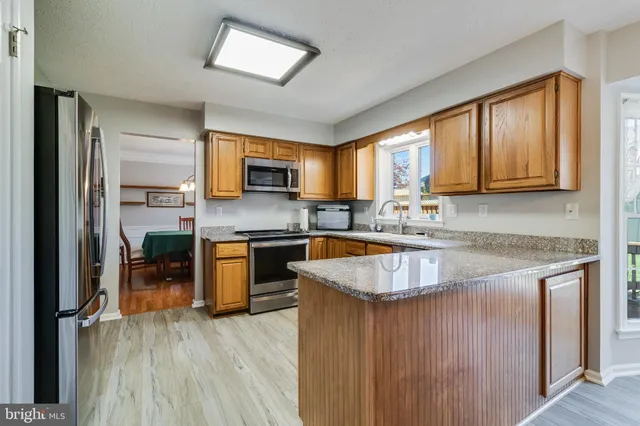 a kitchen with stainless steel appliances granite countertop wooden cabinets a stove top oven a sink and dishwasher with wooden floor