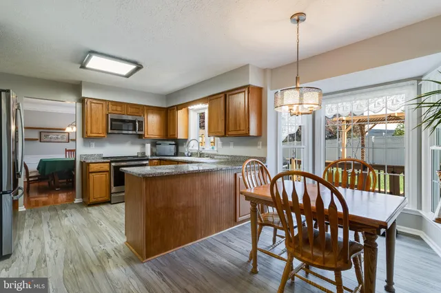 a kitchen with stainless steel appliances granite countertop a stove a sink a refrigerator a dining table and chairs with wooden floor