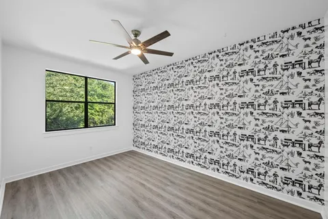an empty room with wooden floor fan and windows