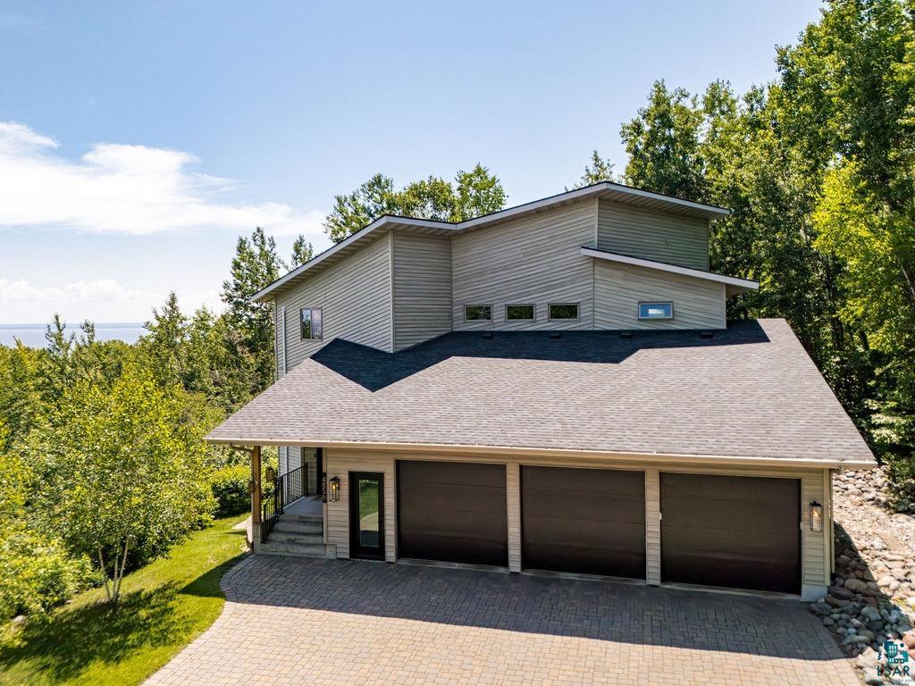 4856 Kingston Street Duluth, MN 55804 - Photo 79 of 88 Modern multi-level residence featuring horizontal siding, a three-car garage with dark paneled doors, and an expansive paver driveway