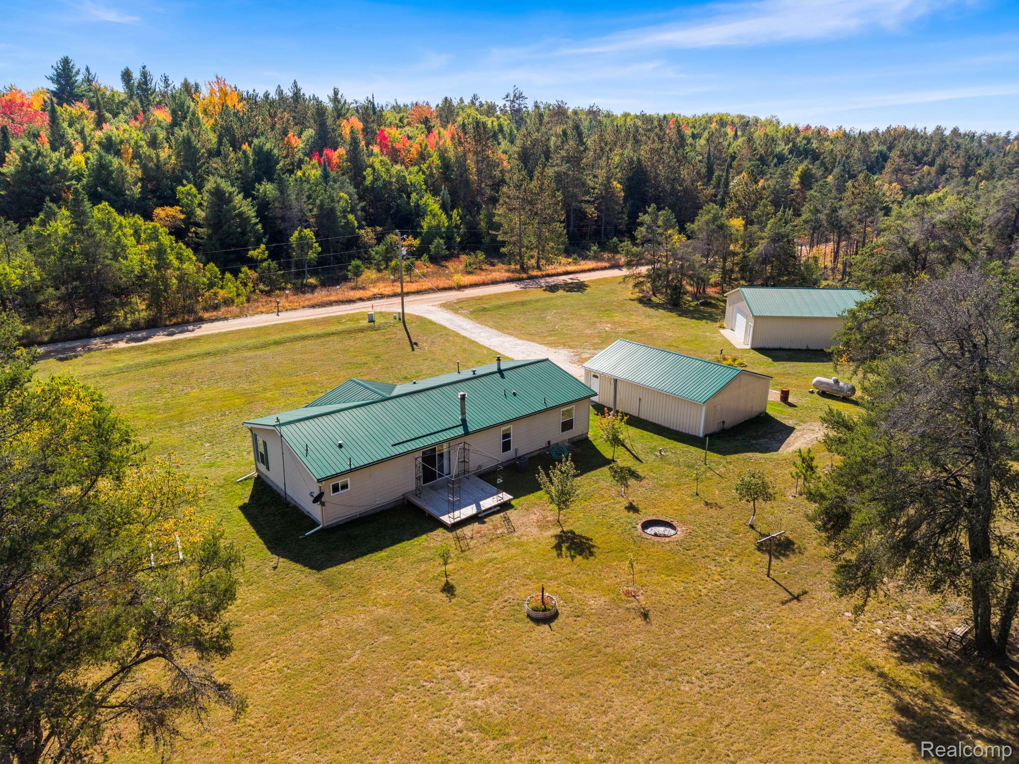 Expansive property featuring a single-story residence with a green metal roof, two detached outbuildings with green metal roofs, and a gravel driveway