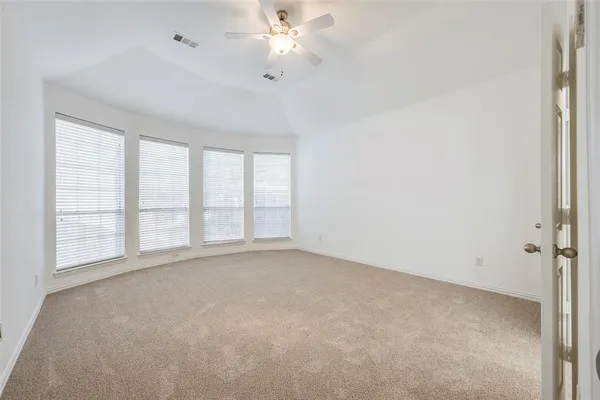 an empty room with chandelier fan and windows