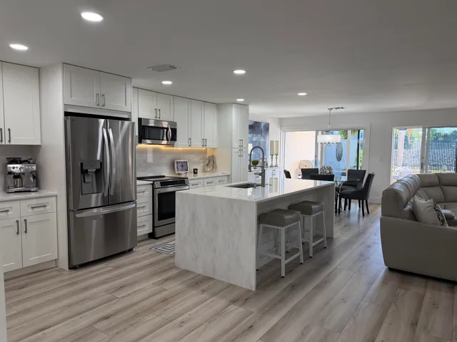 a large kitchen with stainless steel appliances a refrigerator a stove a sink dishwasher and a dining table with wooden floor