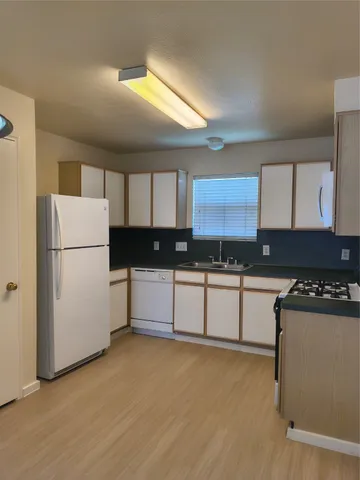 a kitchen with granite countertop a refrigerator a sink and white cabinets