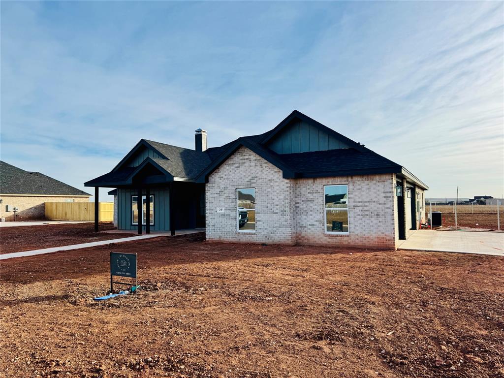 View of front facade featuring board and batten siding, brick siding, a chimney, driveway, and covered porch