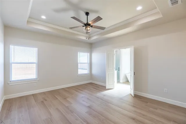 an empty room with wooden floor ceiling fan and windows