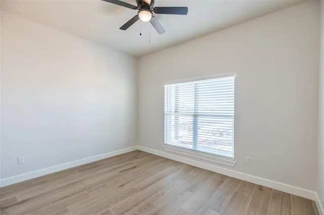 an empty room with wooden floor fan and windows