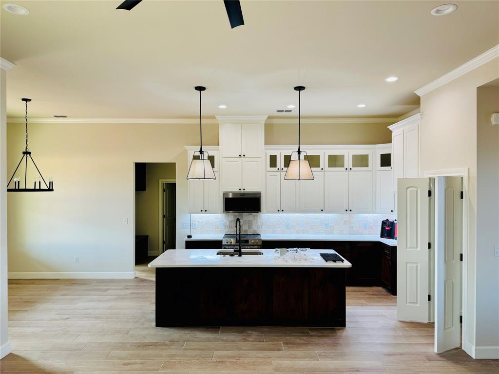 245 Indian Ridge Road Tuscola, TX 79562 - Photo 9 of 21 Kitchen featuring white cabinets, glass insert cabinets, ornamental molding, a center island with sink, and dark brown cabinetry